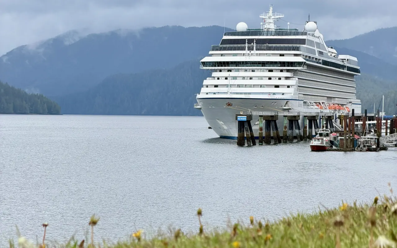 A cruise ship berthed below forested mountains